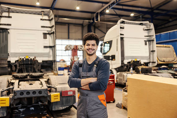 istock Professional confident multiracial serviceman standing with arms crossed in garage with trucks in background. 2192223524