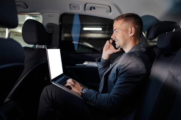 istock Young busy executive is sitting at backseat in a car and having an important phone call while typing on a laptop. 2192224282