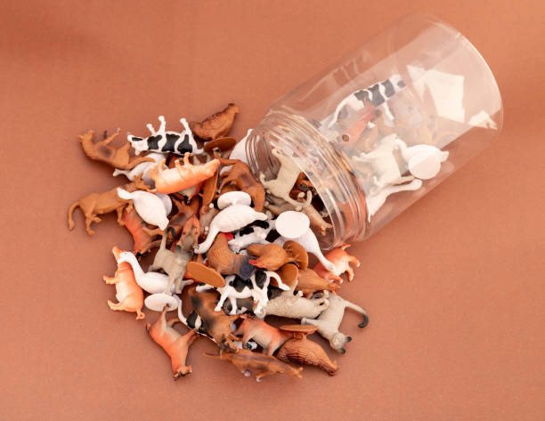 Plastic animal figurines spilled from a transparent jar on brown background