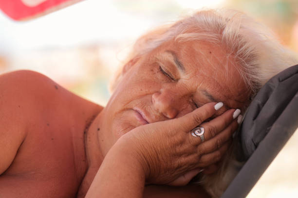 A serene senior lady with gray hair enjoying a restful nap on a beach chair under the sun.