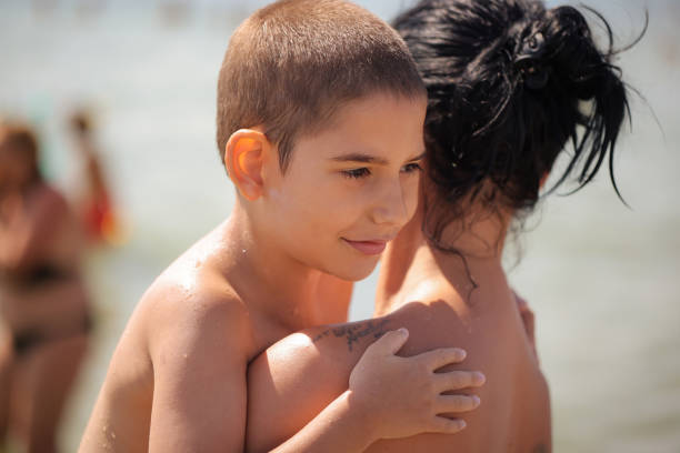 A heartfelt moment of a mom embracing her son with special needs, standing together on the beach.