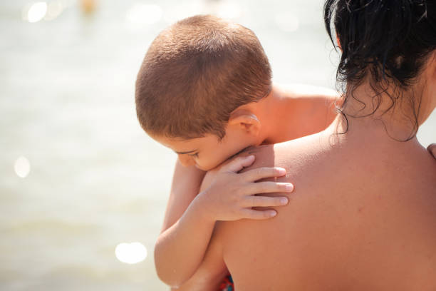 A loving mother holds her son close while enjoying the tranquility of the seaside.