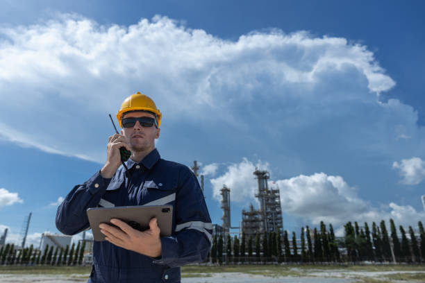 istock Man professional engineer technician wear safety uniform and white hard hat holding tablet and walkie-talkie working area near refining oil petrochemical industry. Factory site energy power station. 2192235525