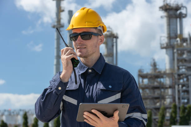 istock Man professional engineer technician wear safety uniform and white hard hat holding tablet and walkie-talkie working area near refining oil petrochemical industry. Factory site energy power station. 2192235559
