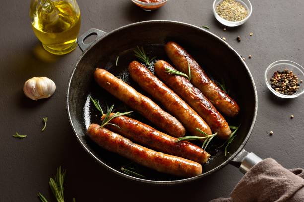 istock Delicious thin sausages in frying pan on dark background 2192236592