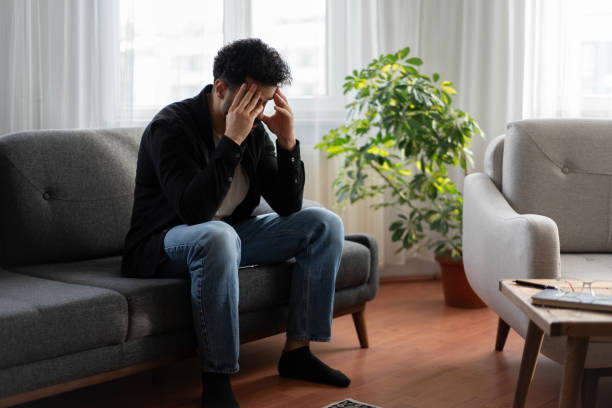 istock Stressed young man suffering from headache sitting on sofa at home 2192252517