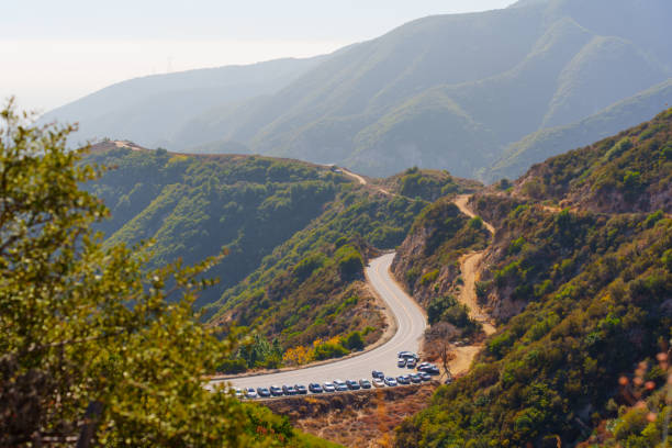 Winding road in La Canada Flintridge, lined with parked cars of nature lovers, surrounded by breathtaking mountainous scenery.