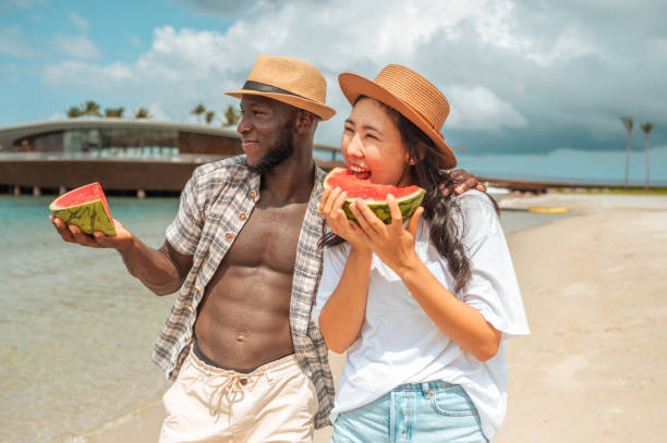 istock Joyful Diverse Couple Savors Watermelon on Beach Retreat 2192257943