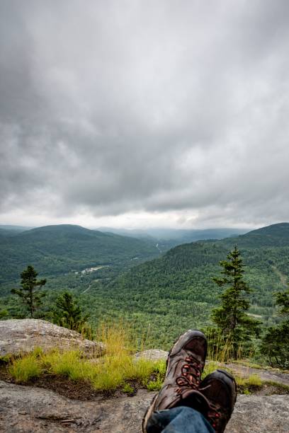 istock Person relaxing on a mountain cliff with hiking boots overlooking a green valley under a cloudy sky. 2192259831