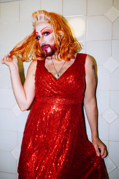 A drag queen showcases bold elegance while posing in a dazzling red sequined dress. This striking look is completed by dramatic makeup and styled hair, capturing the essence of performance art.
