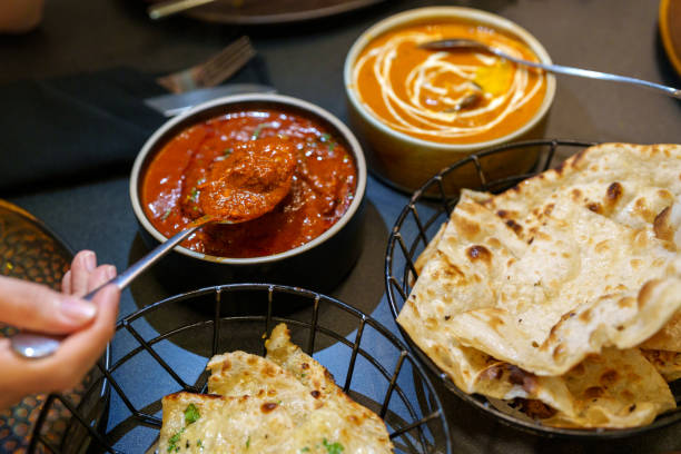 A delicious and comforting scene showcasing an Indian meal with butter chicken and naan. The rich and creamy butter chicken is served in a bowl with a smooth, thick gravy, garnished with cilantro. The naan, soft and slightly charred, is placed in a basket.