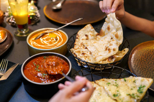 A delicious and comforting scene showcasing an Indian meal with butter chicken and naan. The rich and creamy butter chicken is served in a bowl with a smooth, thick gravy, garnished with cilantro. The naan, soft and slightly charred, is placed in a basket.