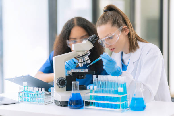 istock Two beautiful female doctors sitting at a table in a science lab with test flasks. Colorful glass bottles filled with various liquids on table with microscope 2192268369