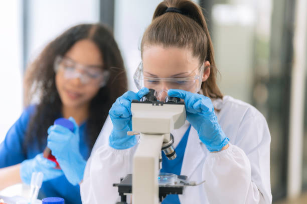 istock Two beautiful female doctors sitting at a table in a science lab with test flasks. Colorful glass bottles filled with various liquids on table with microscope 2192268387