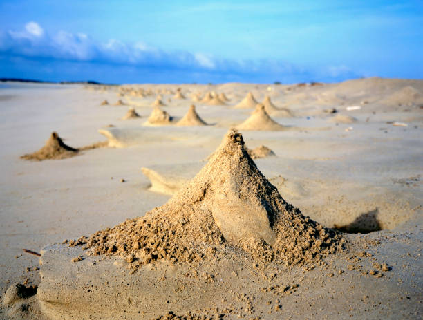 Sand mountain against the ocean and a blue sky with clouds. Dune in the desert. An oasis under the sky - photo of a sand dune against a blue sky with white clouds. Small grains of sand. Dune background. The wind blew away the sand. Clouds in the sky. A mountain of sand and the sky. A large sand mountain against the sea and a blue sky with white clouds. Beach of the sea with sand dunes.