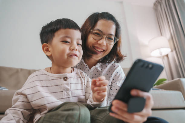 istock Asian Mother and Child Share a Joyful Moment While Watching a Mobile Device at Home in a Comfortable Living Room 2192271156