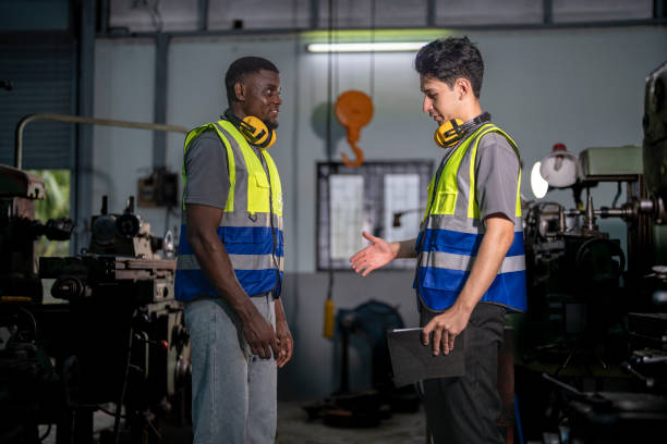 istock Two industrial engineers in high-visibility vests collaborate in a workshop. One holds tablet, pointing at equipment, discussing plans. Ear protection and gloves emphasize safety and professionalism. 2192271454