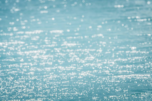 defocused glittering sunlights over blue water surface on a summer day, abstract empty nature background for travel and vacation with copy space