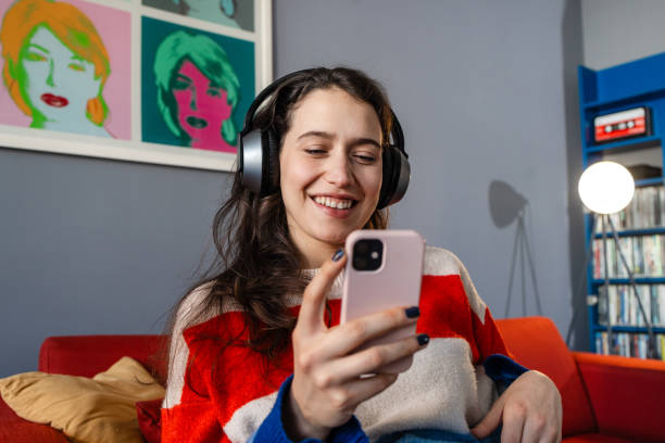 istock Young woman with headphones smiling while using smart phone at home 2192281528