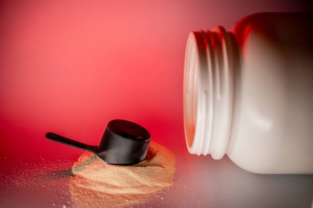 istock Protein powder scoop and container on red background. 2192284105