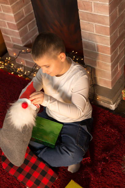 Excited young boy pulling gifts from a stocking by the fireplace