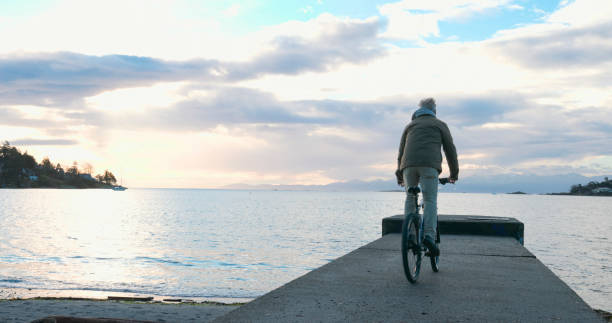 istock Mature man rides bicycle along pier at sunrise 2192296164