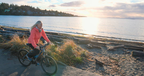 Mature woman bicycles along beach at sunrise