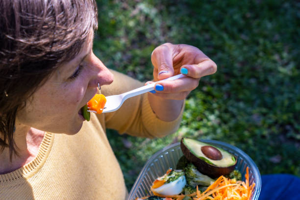 A person takes a bite of colorful salad while seated on the grass, basking in the warm sun.