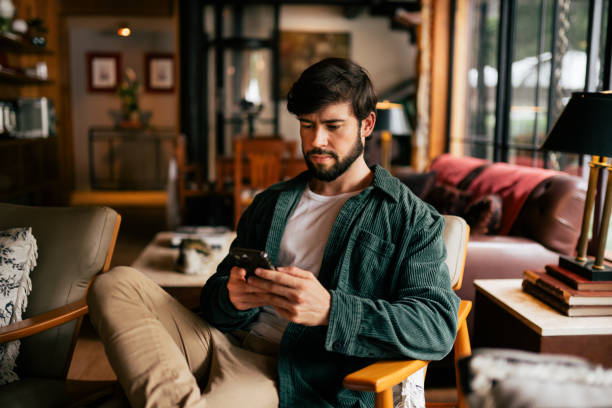 istock Young man using cell phone in the living room 2192318408