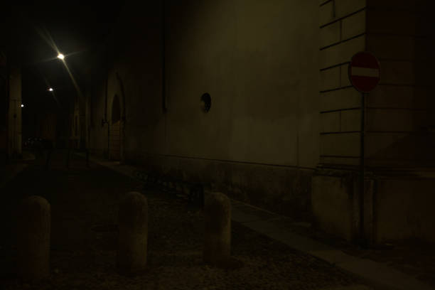 Corner of a cobbled street blocked by concrete pillars in an italian town at night