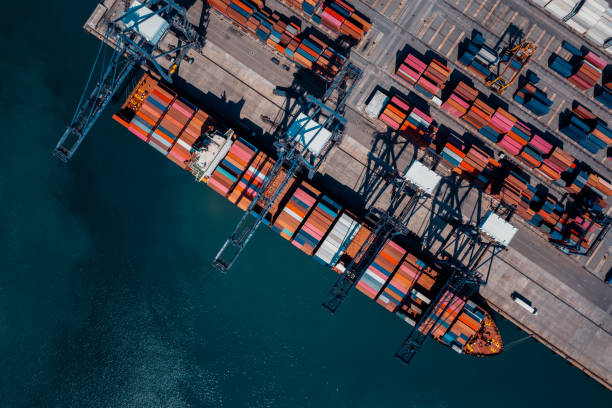 istock commercial port in deep sea load and unloading cargo from container ship import export by crane for distributing goods by trailers transport logistic  to customers and dealers, aerial top view 2192360458