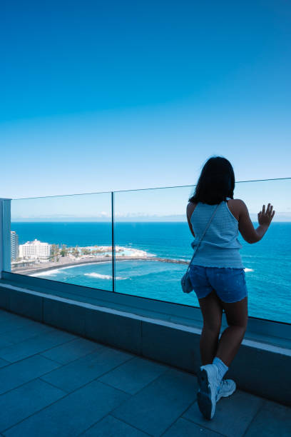 istock A woman stands on a balcony overlooking the ocean. 2192375740