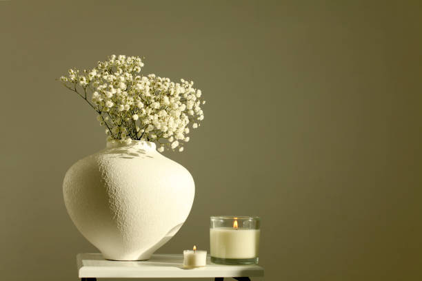 istock Evening still life. Flower bouquet in bowl and burning candle on beige interior. Selective soft focus. Minimalist still life. Light and shadow nature background. 2192382641