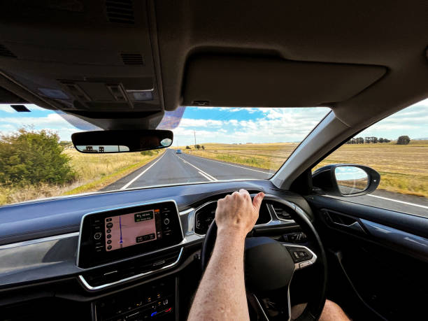 istock A wide-angle view through a car’s windscreen reveals a highway through a desert plain, framed by the interior, steering wheel, and driver’s hands under a clear blue sky with fluffy clouds 2192383911
