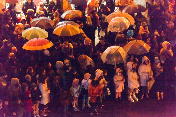 Blurred motion of the crowd. People are excited during street rock concert. Rain in tonight. Umbrellas. They dance. Bright blue neon  lighting. Night life of the big city. Back view
