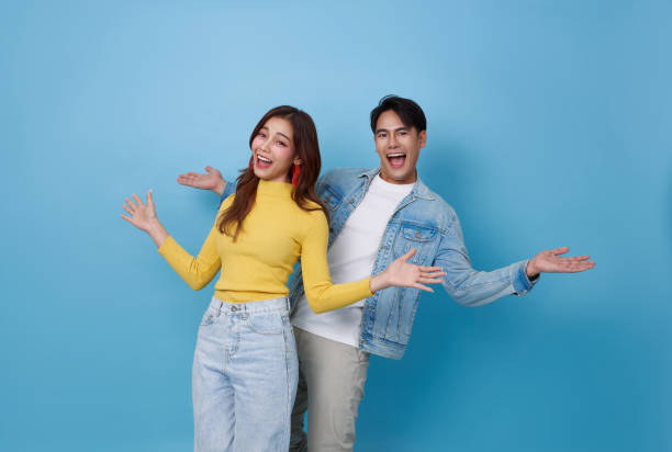 istock Surprised Asian couple standing smiling and opening hands isolated on blue studio background. 2192392498