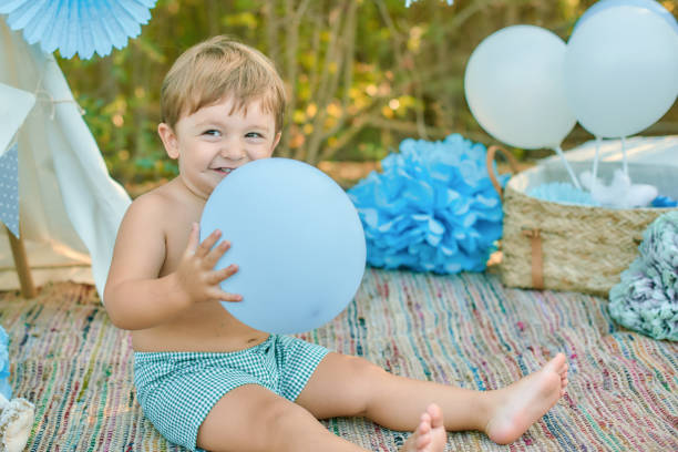 A little boy with an armful of balloons walks in the autumn park. Yellow trees and blue balls. Stylish child.