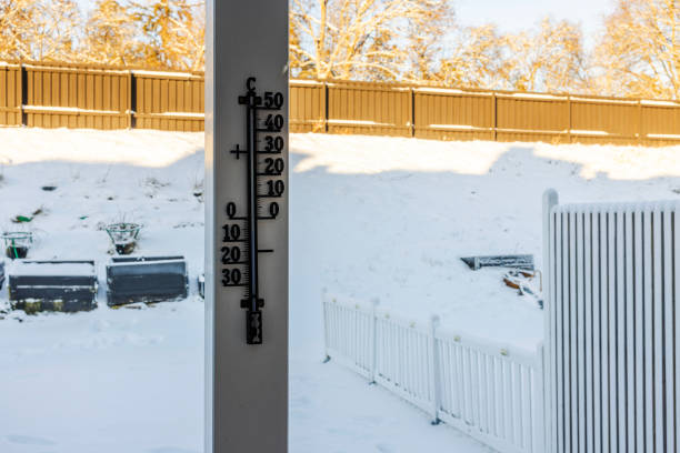 Outdoor thermometer on wooden post shows subzero temperature against snowy backyard with raised garden beds and white fence. Sweden.
