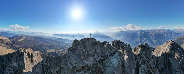 A stunning panorama showcasing a sunlit rocky mountain ridge surrounded by expansive alpine landscapes under a clear blue sky. Perfect for themes of exploration, nature, and high-altitude serenity.