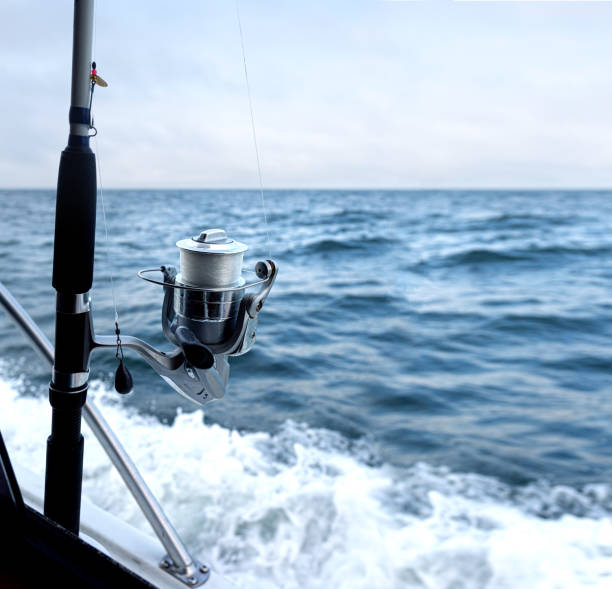 Fishing rod spinning with the line over blue sea. Fishing rod in rod holder in boat. Copy space