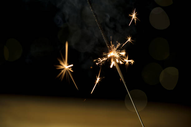 Sparkler, small wire stick firework, throwing off brilliant sparks on New Year's Eve, close up shot. Celebration concept.