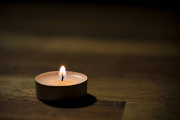 Small white tea candle on a wooden table, close up shot. Tealight ambiance concept.