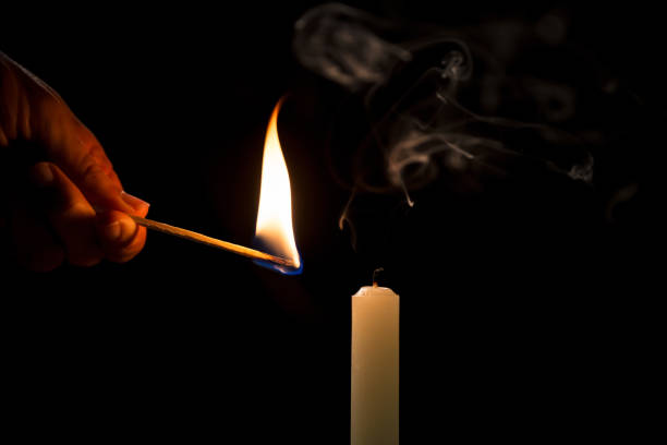 istock Male hand lighting a white candle with a match, on a black background 2192414774