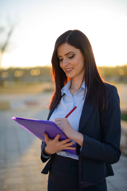 Young professional woman with red glasses writing on notepad in an urban setting, showcasing productivity and focus in a casual environment