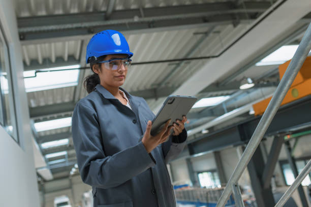 istock Woman with blue helmet, an engineering programmer at a factory looking at tablet 2192435400