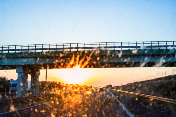 Highway and bridge at sunset through a dirty windshield, emphasizing road safety and the challenges of visibility while driving on long journeys. Transportation, logistics, road traffic. Copy space