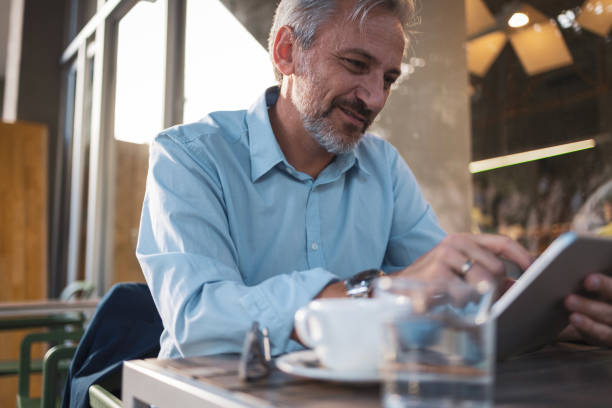 istock Mature man reviewing financial documents on tablet at cozy cafe setting 2192440771