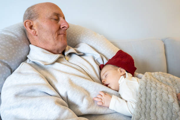 Stockholm, Sweden A  middle aged man  sleeps on the couch with his newborn granddaughter.