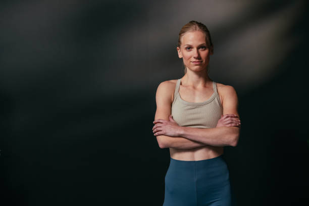 Confident young woman with arms crossed posing on dark background