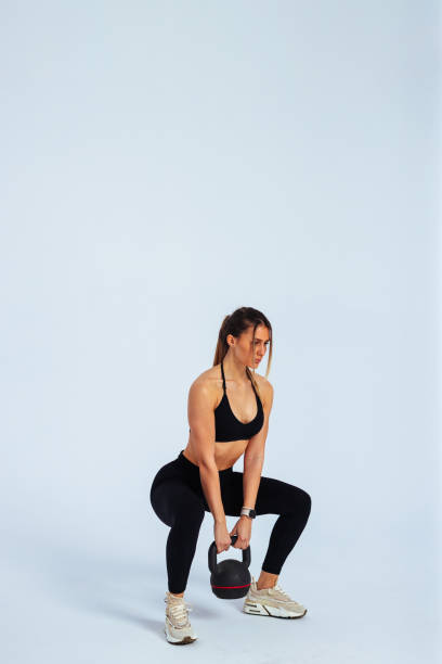 istock Young athletic woman performing kettlebell squats on white background 2192441126